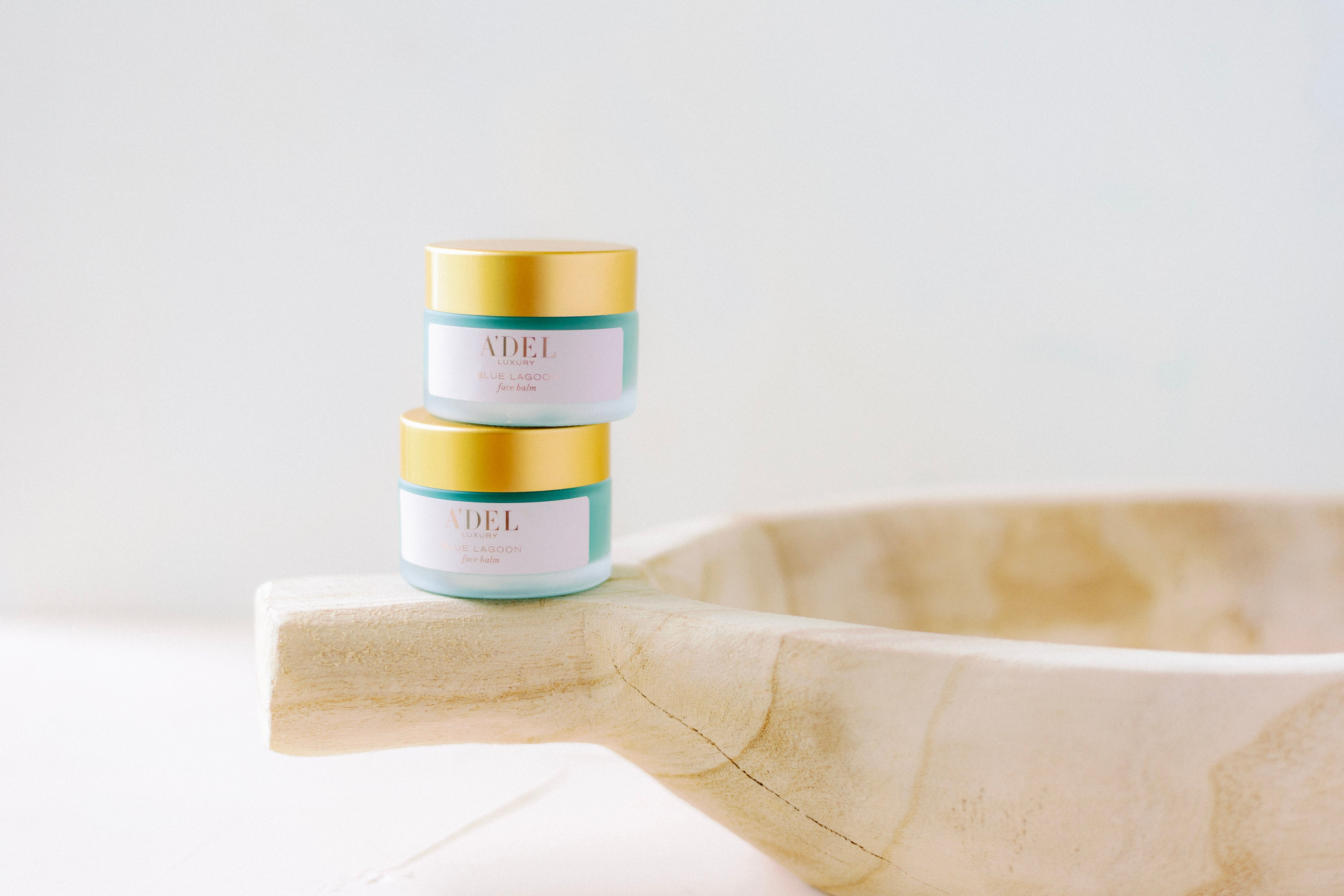 2 1 oz each blue lagoon face balm stacked on top of each other balancing on the handle of a wooden bowl.