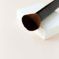 A black makeup brush with brown bristles that come to a flat, blunt shape on top. The bristles are medium to dense packed. The brush is facing the camera showing how dense the bristles are packed. 