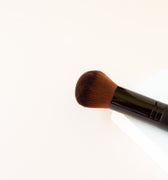 A white background with the top half of a black makeup brush with brown bristles that come to a dome shape on top. The bristles are medium to dense packed. 