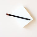 A slightly tapered brush laying on a white block on on peach background