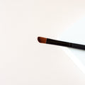 narrow makeup brush with a slight taper on one side to give it an angle sitting on a white background