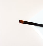 narrow makeup brush with a slight taper on one side to give it an angle sitting on a white background